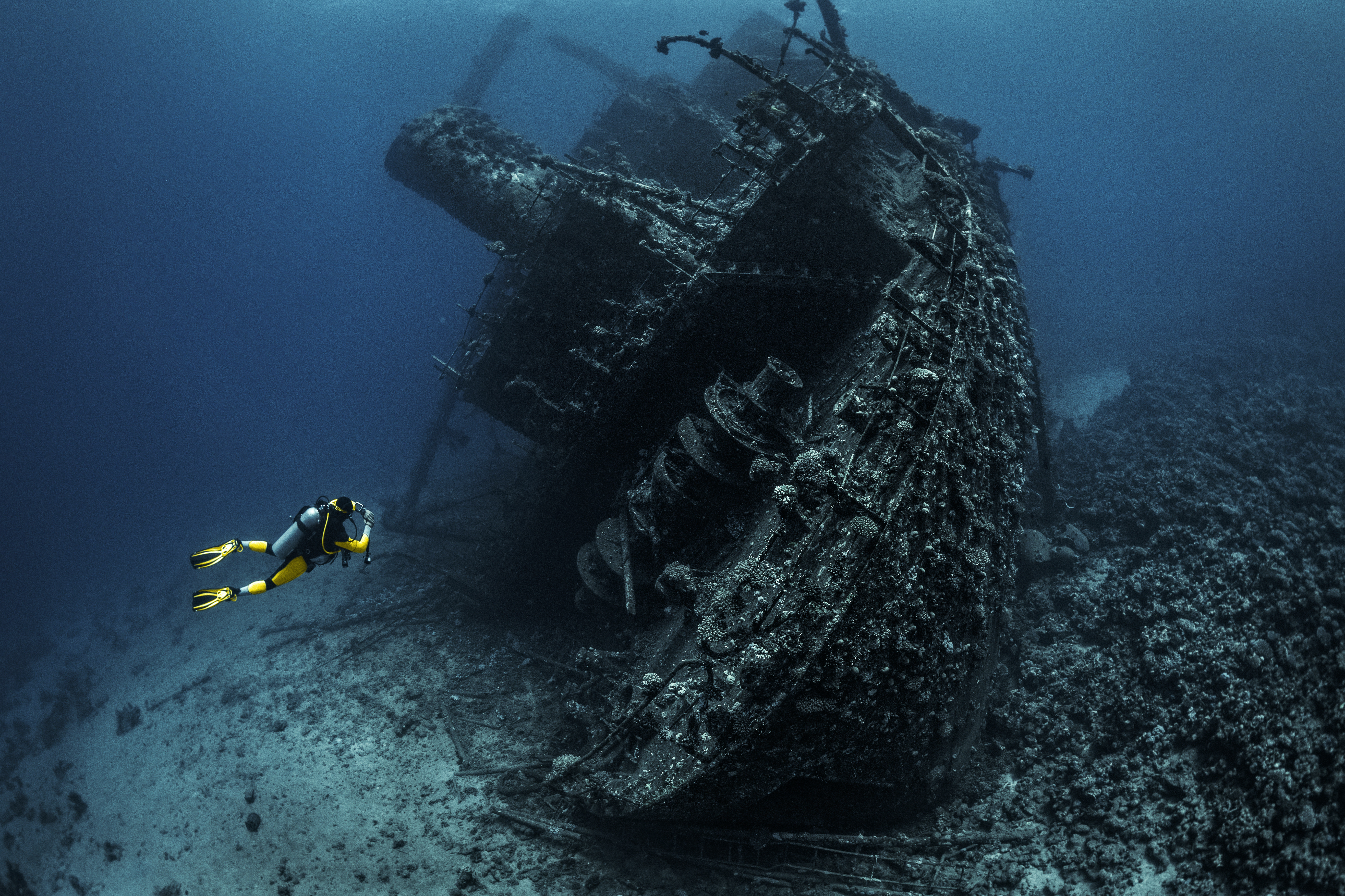Scuba diver observing a large shipwreck completely rusted and overgrown lying underwater in the Red Sea - stock photo